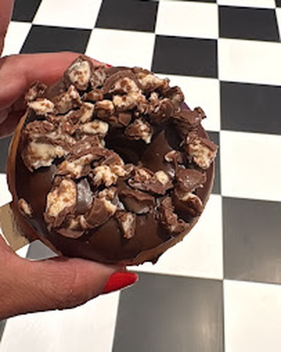 Donut au chocolat avec éclats de Daim, tenu en main devant le damier noir et blanc du diner
